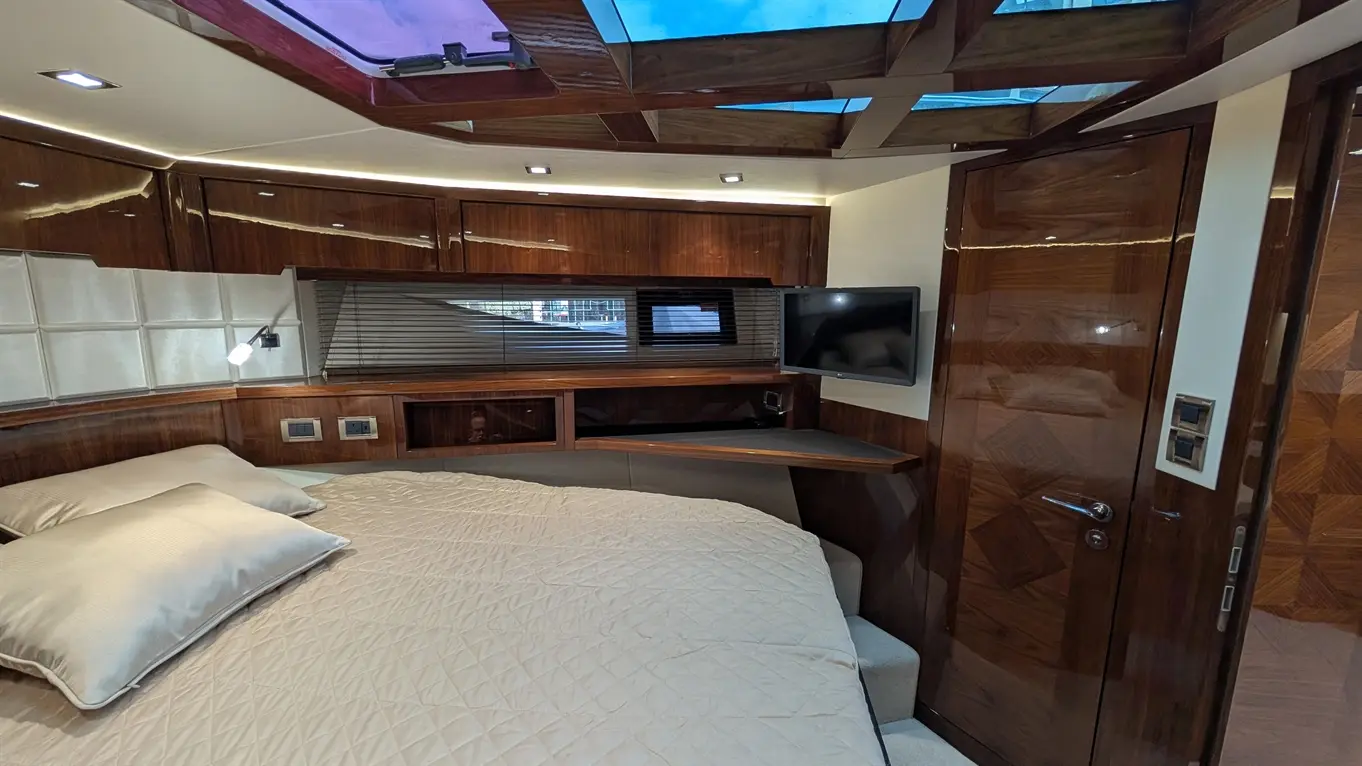Luxurious boat interior featuring a double bed, wood paneling, a TV, and a skylight, complemented by elegant lighting.